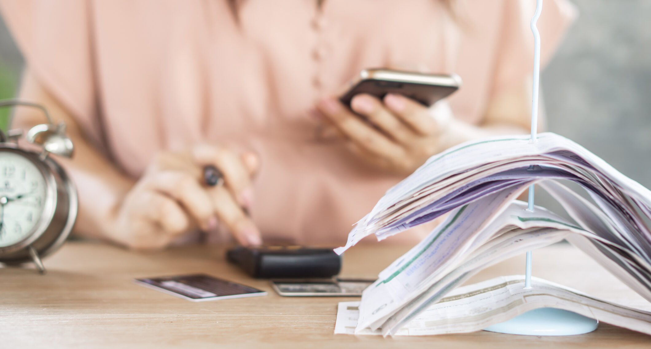 Woman reviewing receipts, counting on her phone and a calculator