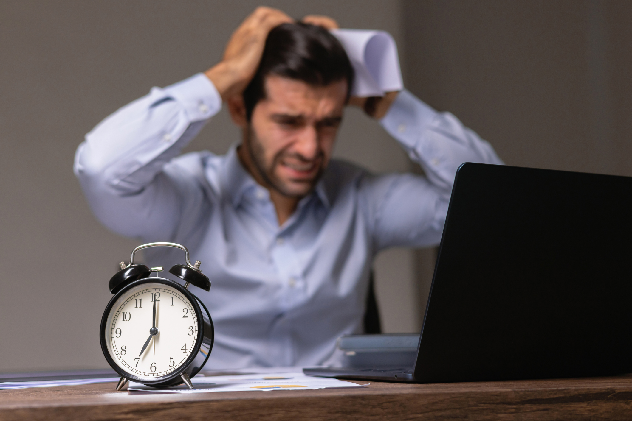 Man sitting at his desk in a state of panic with an alarm clock about to go off